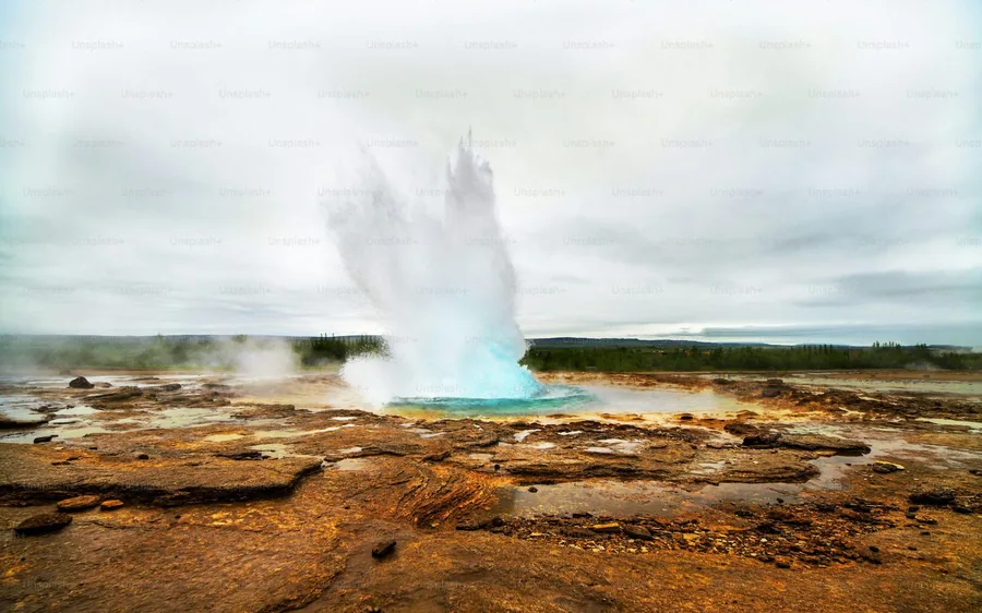 A geyser erupting on the orange mineral ground of the Haukadalur field