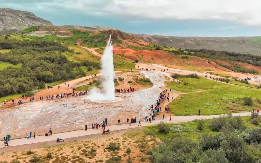Strokkur erupting seen from above with the red hillside behind