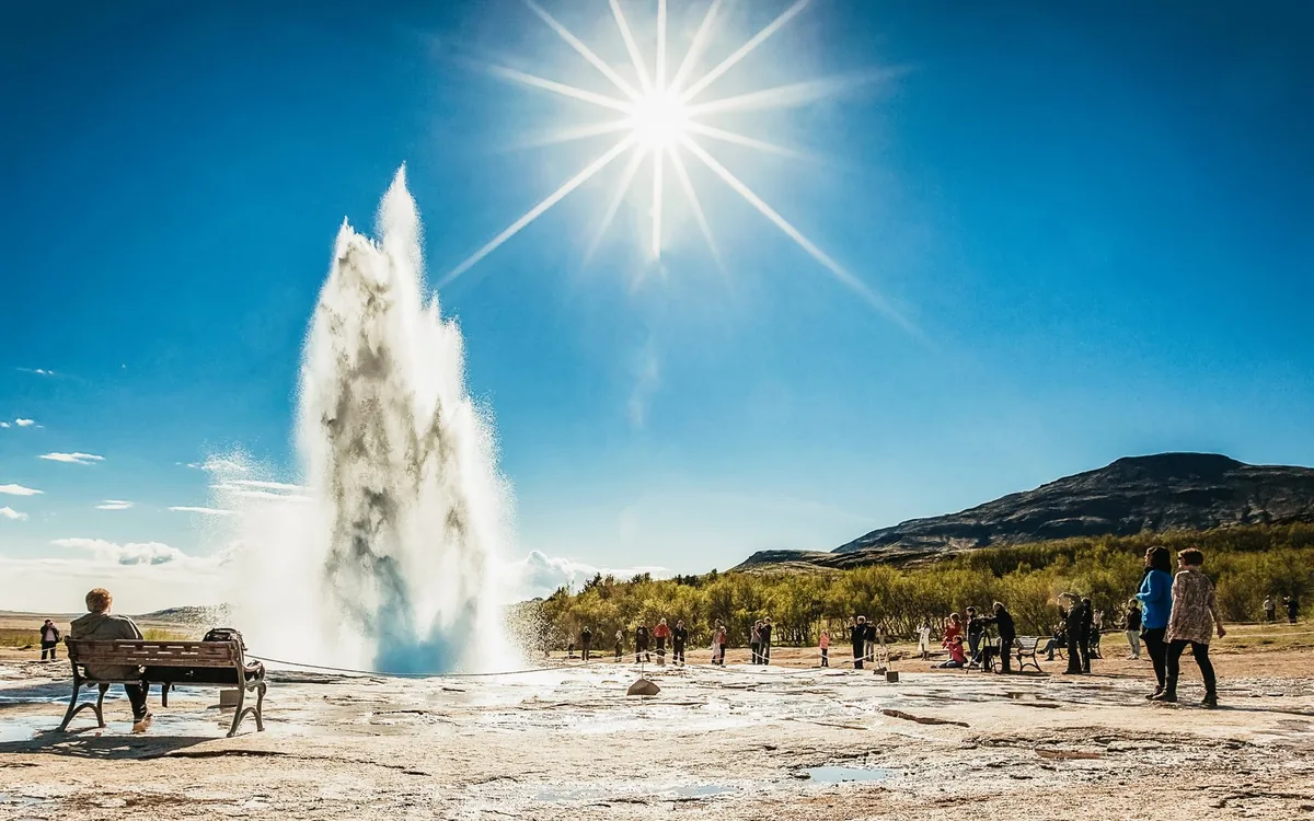Strokkur geyser erupting in front of a crowd of visitors